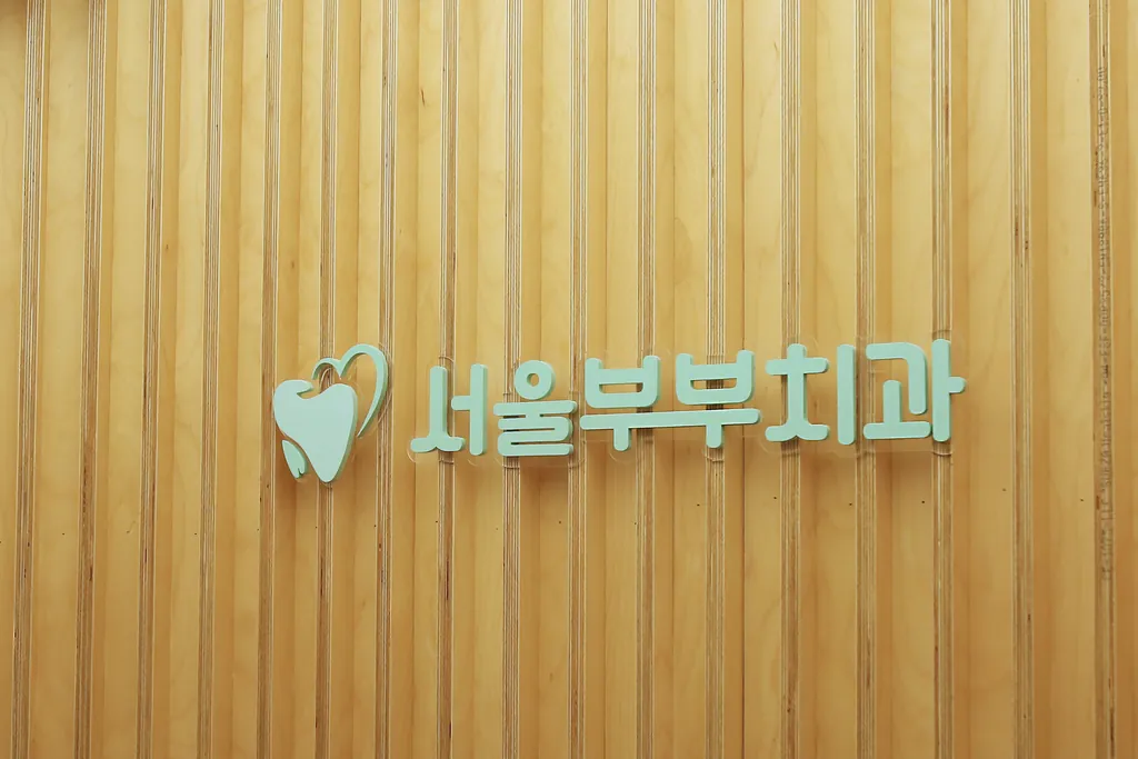 원목 루버 벽에 붙은 민트색 서울부부치과 로고